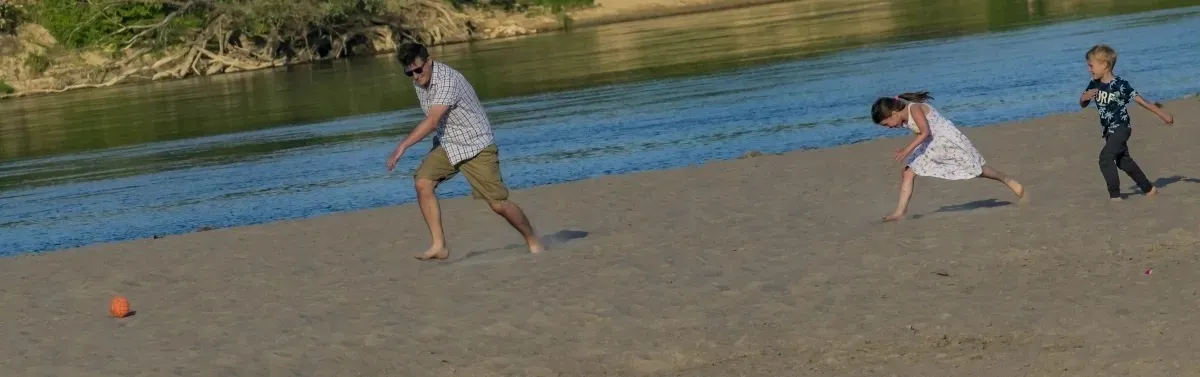 Adult and two children running across a sandy riverside